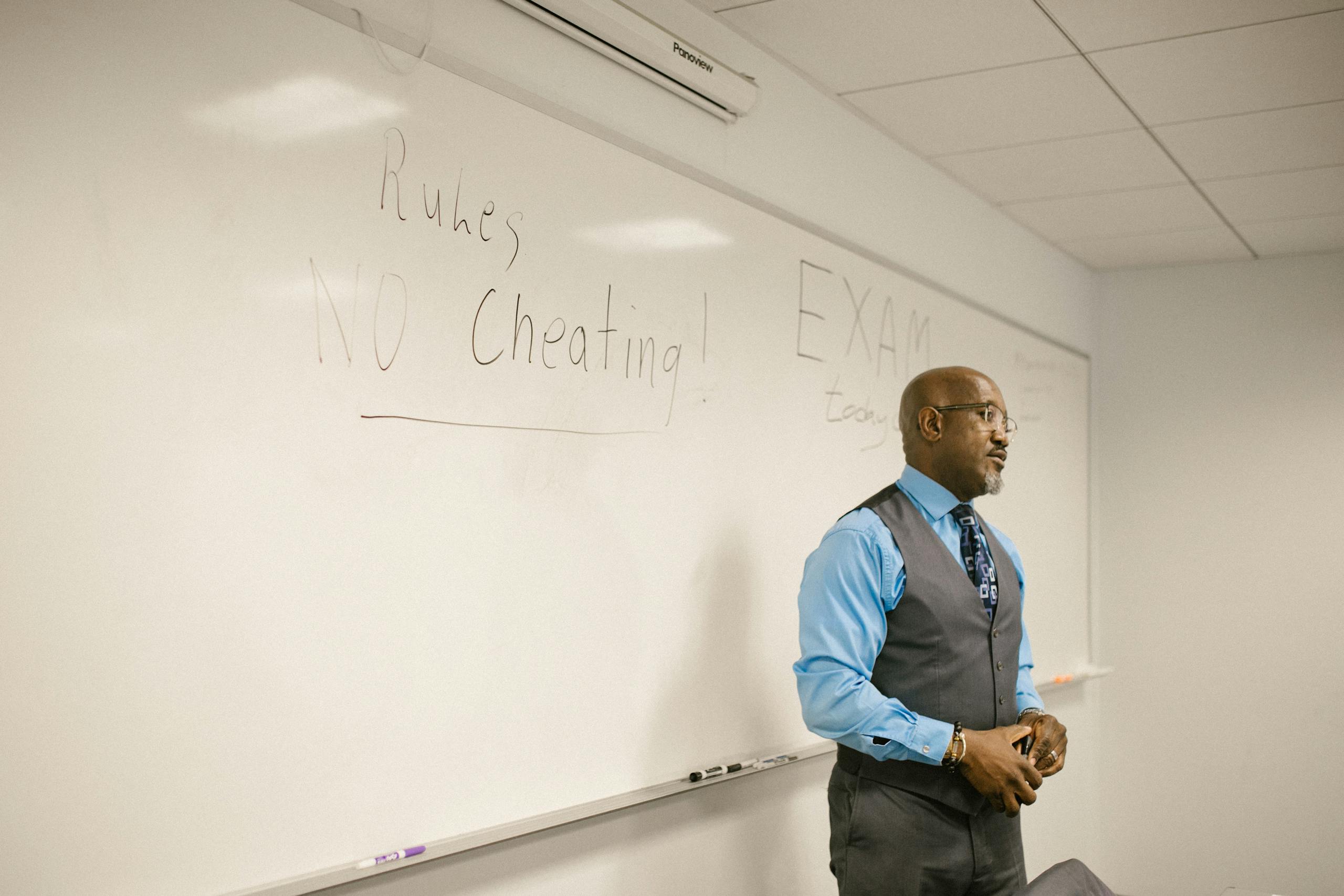 A professor in a classroom emphasizing exam rules on a whiteboard.